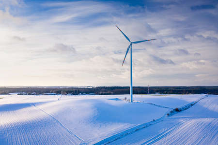Snowy field and wind turbine at sunrise in winter. Aerial view of nature in winter.