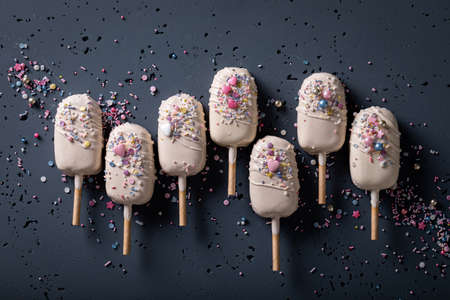 Tasty and sweet ice creams made of white chocolate and sprinkles on dark stone table
