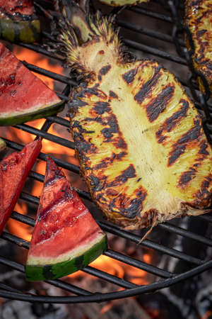 Homemade grilled watermelon and pineapple on bonfire with flames. Roasted watermelon and pineapple on grill.の写真素材
