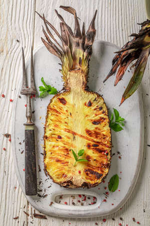Tasty burned pineapple with herbs and pepper. Roasted pineapple on grill with flames.の写真素材