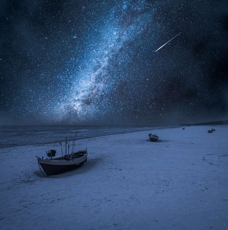 Milky way and falling stars over boats by Baltic Sea. Baltic Sea in winter at night.