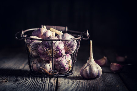 Fresh and healthy garlic in old metal basket on wooden tableの写真素材