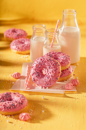 Tasty and fresh pink donuts as a lunch snack. Best tastes with milk on yellow table. Most popular dessert.の写真素材