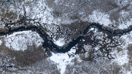 Aerial view of winding river and frozen forest in Poland. The trees are covered with snow.