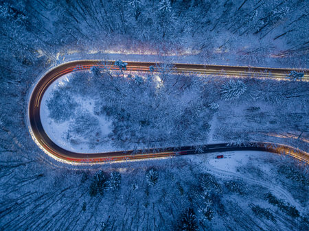 Car headlights illuminating a winding winter road and snowy fores. Transport in winter at night.
