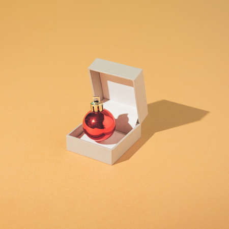Creative and minimal New Year engagement concept with jewelry box and bright red Christmas bauble on sand coloured background. Trendy Vintage aesthetic.の写真素材