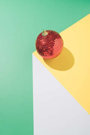 Vintage minimal geometric concept with red Christmas bauble on white, yellow and mint green background. Creative gravity arrangement. New Year party composition.の写真素材
