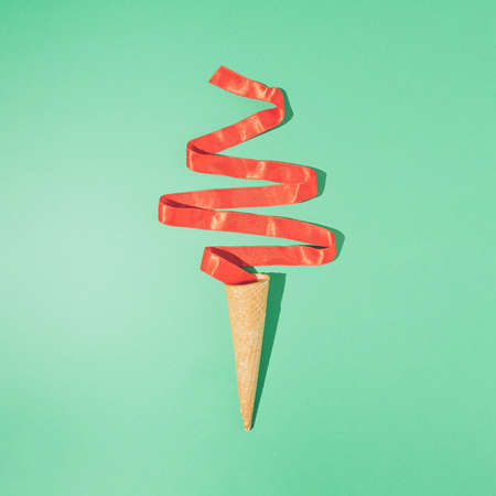 Creative Christmas tree ice cream. Vintage winter holiday concept with cone and red ribbon on mint green background. Minimal New Year party flat lay.の写真素材