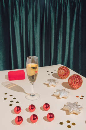 Creative retro aesthetic concept. Minimal New Year party composition with jewelry box, champagne glass, confetti and red Christmas baubles. Modern holiday pattern on green and sand coloured background.の写真素材