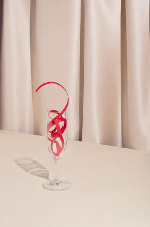 Trendy minimal holiday concept with red decorative Christmas ribbon and champagne glass on elegant silk background. Stylish New Year party aesthetic.の写真素材
