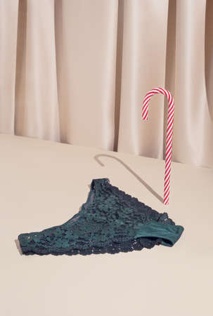 Minimal elegant composition with green lace Christmas panties and candy cane on stylish silk background. Holiday lingerie shopping concept.の写真素材