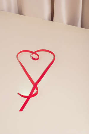 Trendy minimal Valentine's day composition with red ribbon heart on elegent silk background. Modern love concept.の写真素材