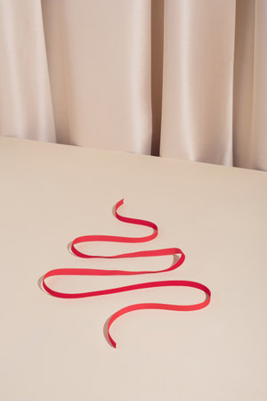 Trendy modern holiday concept with red decorative Christmas tree shaped ribbon on elegant silk background.の写真素材