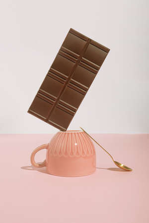Minimal trendy coffee break concept with cup, chocolate bar and teaspoon on pastel pink background. Modern, romantic aesthetic.の写真素材