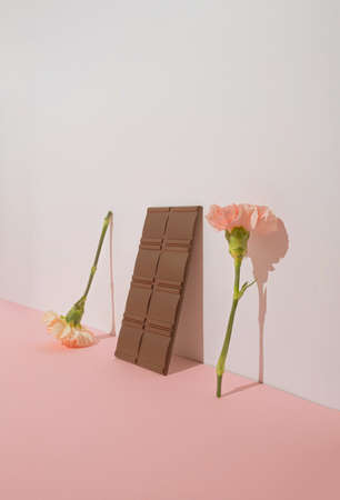 Minimal modern concept with two pink flowers and chocolate on pastel background. Trendy aesthetic with copy space.の写真素材