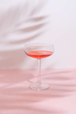 Romantic composition with red wine glass and leaf shadow on pastel pink background on a sunny day. Trendy, minimal party concept.の写真素材