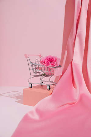 Minimal trendy Valentine's day shopping concept with pastel pink rose and cart. Modern romantic aesthetic.の写真素材