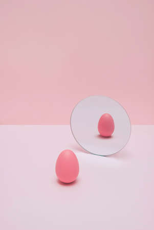 Trendy pastel pink Easter concept with coloured egg and mirror reflection. Fun, romantic and minimal aesthetic.の写真素材