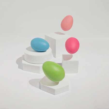 Bright and fun Easter concept with four colorful eggs jumping from white blocks. Trendy, minimal spring aesthetic.の写真素材
