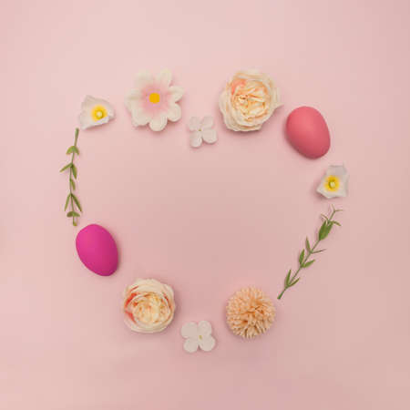 Pastel heart shape made of Easter eggs and colorful spring flowers on pink background. Minimal style concept.の写真素材