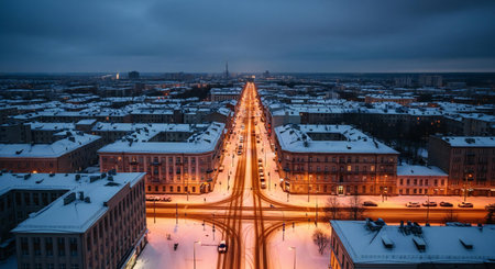 An aerial view of a snow-covered city street at dusk, with buildings and a central road glowing with warm lights.の素材
