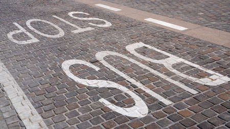 Bus stop sign painted in white color on the tiles on the road.