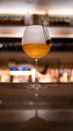 A glass of white wine cocktail on a bar with yellow lights