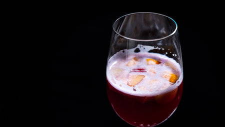 A glass of red wine with a slice of peach on a black backgroundの写真素材