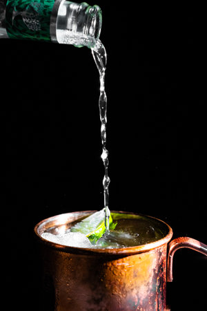Pouring fresh mint into a copper pot with ice cubes on black backgroundの写真素材