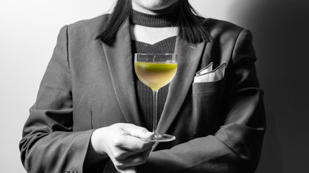 Woman in a black suit with a glass of cocktail on a white backgroundの写真素材