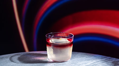 cocktail in a glass on a table on a background of colored lightsの写真素材