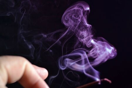 Hand holds a stick of incense game of smoke on a dark backgroundの写真素材