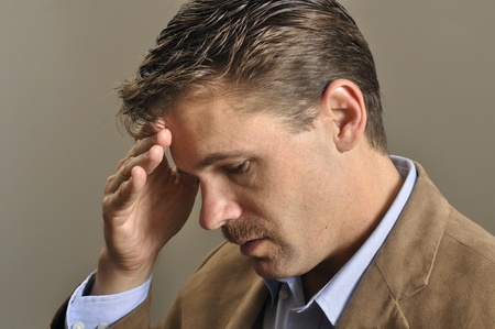 Closeup of depressed man looking down with hand on faceの写真素材