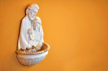 Sculpted holy water dish of the blessed family on orange wall in Catholic church