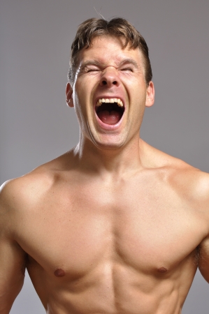 Strong shirtless man screams while he flexes musclesの写真素材