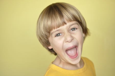 Closeup of young blonde boy screaming on yellow backgroundの写真素材