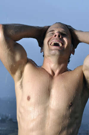 Muscular shirtless man laughing outside in rainの写真素材