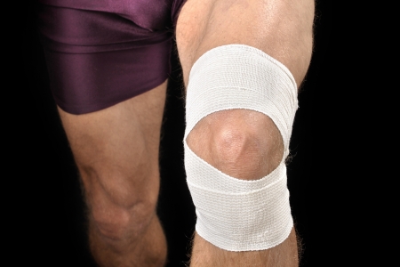 Front closeup of knee of athletic man with white sports wrap on black backgroundの写真素材