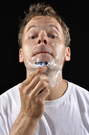 Portrait of Caucasian man shaving chin with sharp razor on black backgroundの写真素材