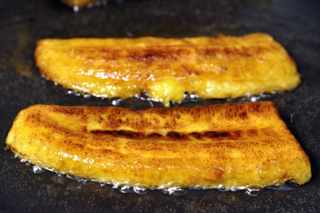 Closeup of crisp yellow sliced plantain bananas frying in pan with hot oilの写真素材
