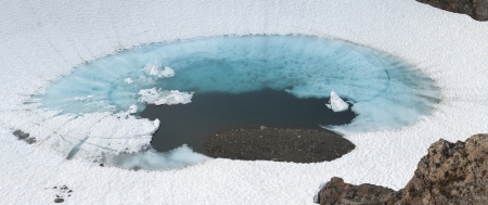 Beautiful panoramic of deep blue glacial pool surrounded by white snow on Bear Mountain in Alaska