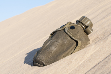 Green army canteen sits half buried in desert sand dune on hot sunny dayの写真素材