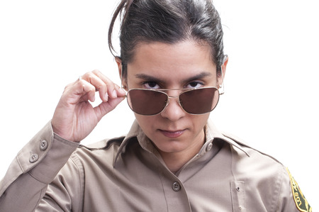 Pretty Hispanic female sheriff deputy dips sunglasses revealing bold penetrating eyes on white backgroundの写真素材