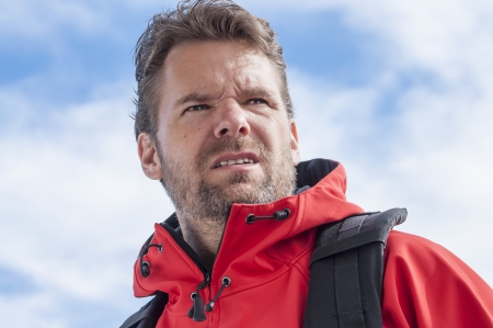 Closeup of determined bearded Caucasian man hiking with intense strenuous expression wearing red jacket and sky in backgroundの写真素材