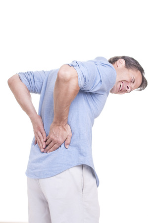 Handsome young Caucasian man in blue shirt struggles with intense back pain on white backgroundの写真素材