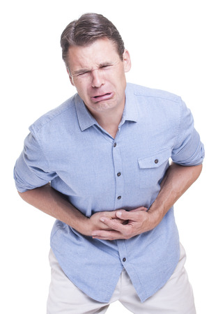 Caucasian man in blue shirt cries in extreme pain while pressing hands against  ache in stomach on white backgroundの写真素材