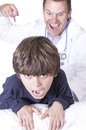 Young Caucasian boy screams in fear as crazy male doctor in white lab coat prepares to plunge needle into childの写真素材