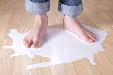 Closeup of child feet standing in spilled milk on wood floorの写真素材