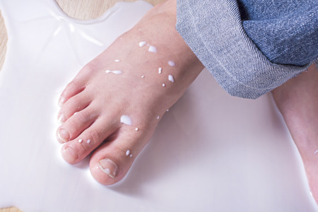 Closeup of young child foot stepping in puddle of spilled milk on floorの写真素材