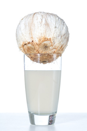 Fresh white coconut sitting on top of glass of coconut water on white backgroundの写真素材